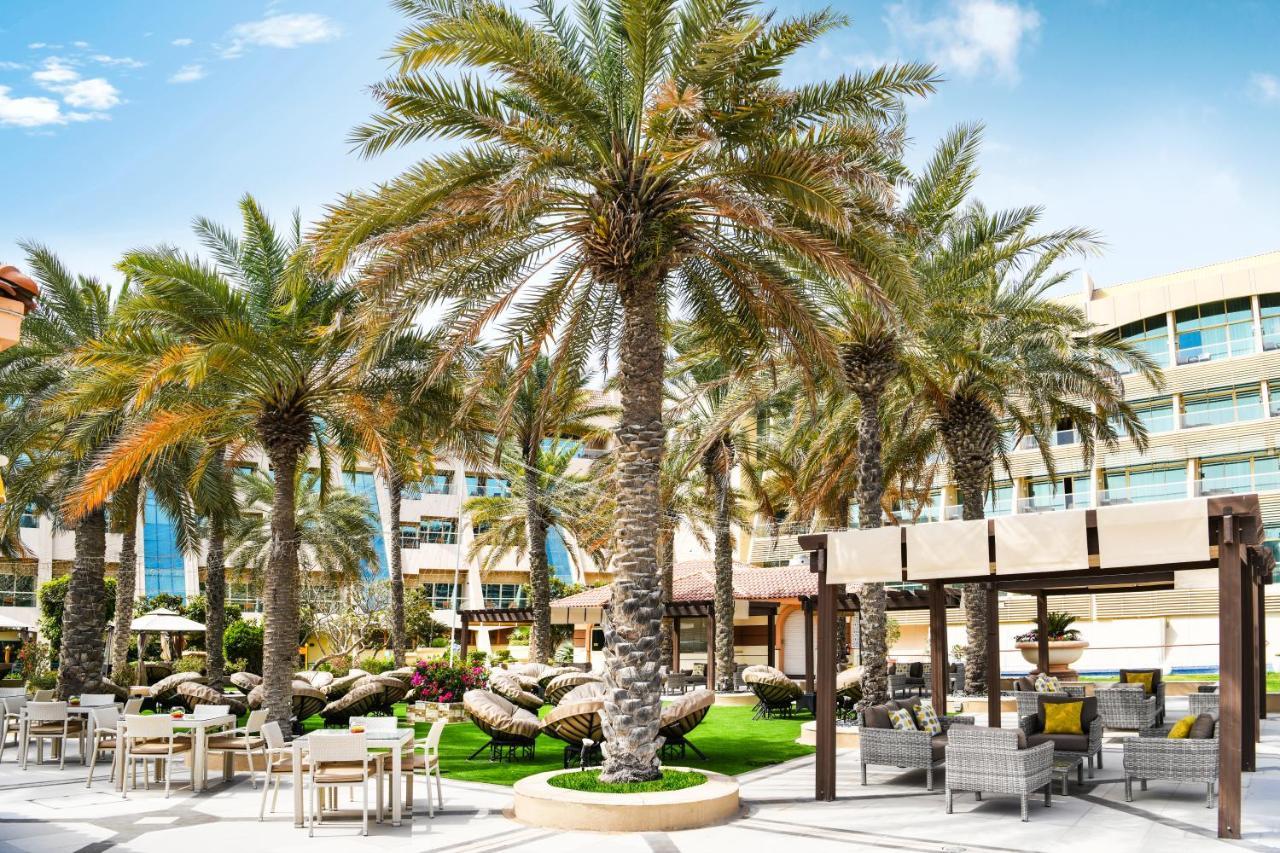 אבו דאבי Al Raha Beach Resort & Spa מראה חיצוני תמונה The photo shows a picturesque outdoor area, likely at a resort or hotel. It features several tall palm trees that provide a tropical feel. In the foreground, there are several lounge chairs and seating arrangements, suggesting a relaxing environment.
