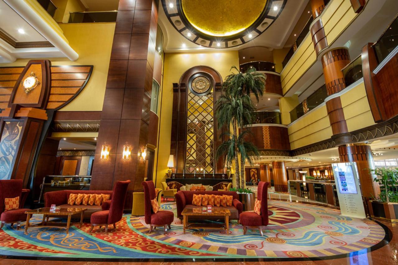 אבו דאבי Al Raha Beach Resort & Spa מראה חיצוני תמונה The photo shows an elegant lobby interior of a hotel. The space features tall ceilings with decorative lighting and large windows, allowing for natural light. There are several plush seating arrangements, including red armchairs and wooden tables, cr