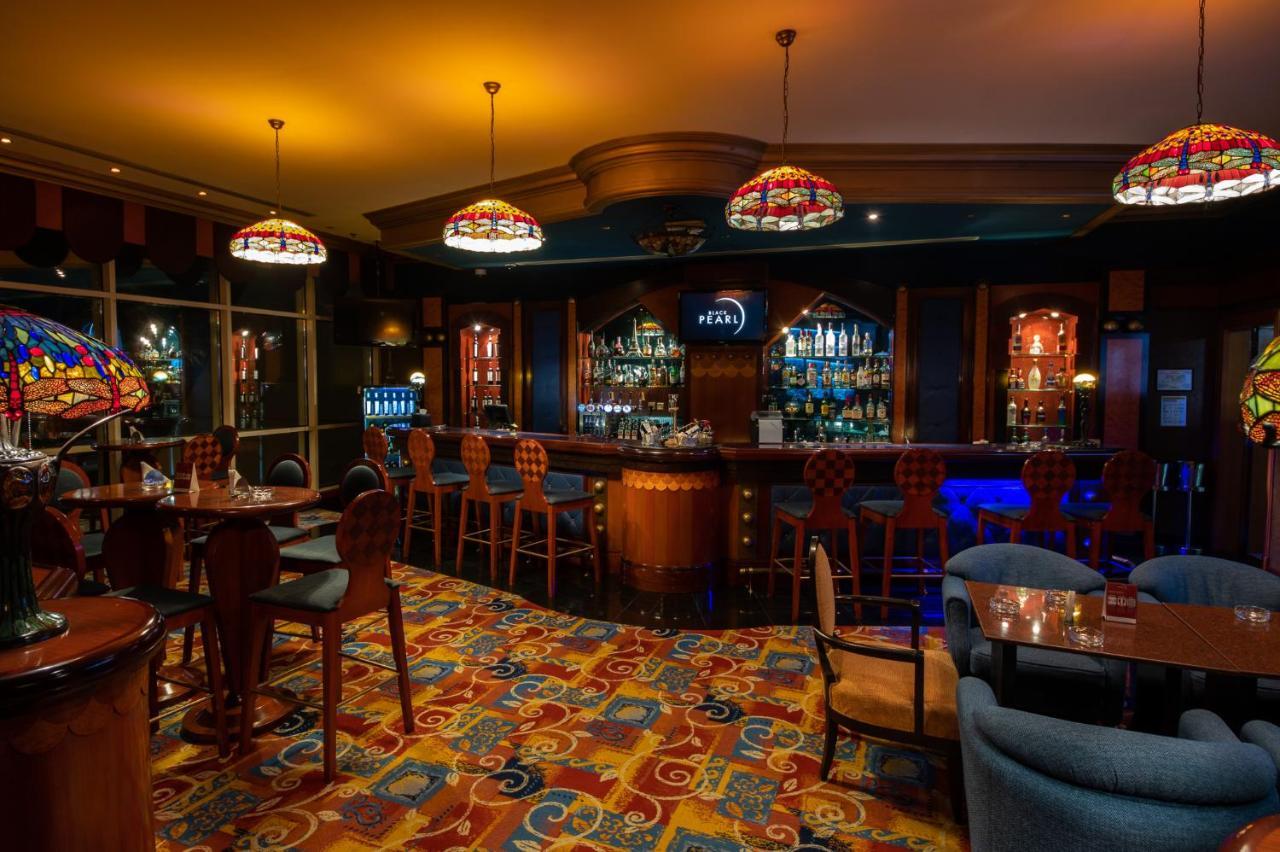 אבו דאבי Al Raha Beach Resort & Spa מראה חיצוני תמונה The photo shows a cozy bar interior, featuring a well-stocked bar area with various bottles displayed on shelves. The bar is illuminated by colorful stained glass light fixtures, creating a warm and inviting atmosphere. The floor is covered with a vi