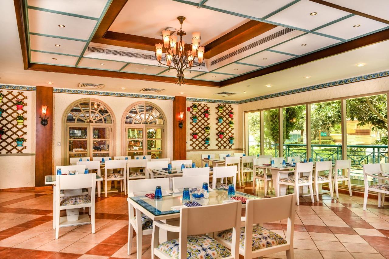 אבו דאבי Al Raha Beach Resort & Spa מראה חיצוני תמונה The photo shows the interior of a restaurant or dining area. The space has a warm and inviting atmosphere, featuring a mix of decorative elements. 

- **Seating**: There are several white wooden tables and chairs arranged throughout the area, some wi