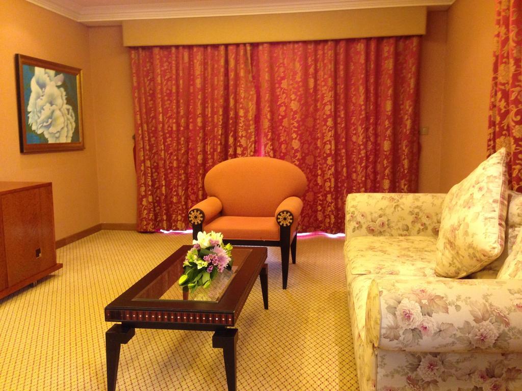 אבו דאבי Al Raha Beach Resort & Spa מראה חיצוני תמונה The photo shows a cozy living room setting. There is an orange chair with decorative armrests situated near a floral-patterned sofa. A coffee table with a floral arrangement sits in front of the sofa. The room is adorned with warm colors, complementi
