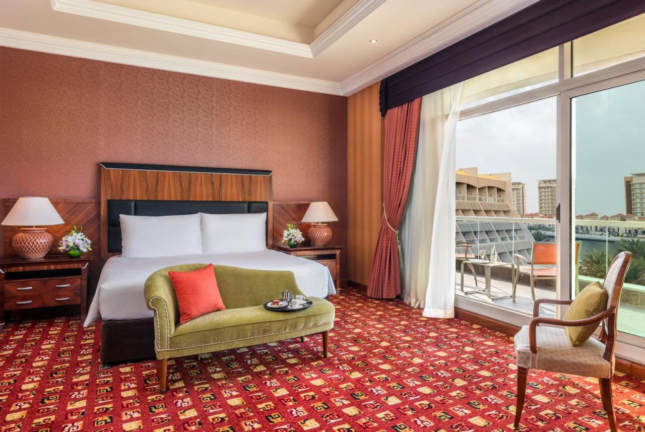 אבו דאבי Al Raha Beach Resort & Spa מראה חיצוני תמונה The photo shows a hotel room with an elegant and modern design. It features a large bed with white linens and a dark wooden headboard. On either side of the bed are matching bedside lamps. There is a green armchair with a red pillow positioned near t