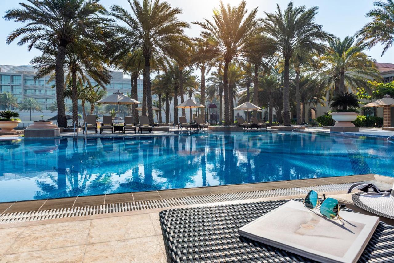 אבו דאבי Al Raha Beach Resort & Spa מראה חיצוני תמונה The photo shows a vibrant swimming pool surrounded by palm trees under a clear sky. The pool's water is sparkling in the sunlight, creating a serene and inviting atmosphere. Lounge chairs are placed around the pool, some of which are shaded by umbrel