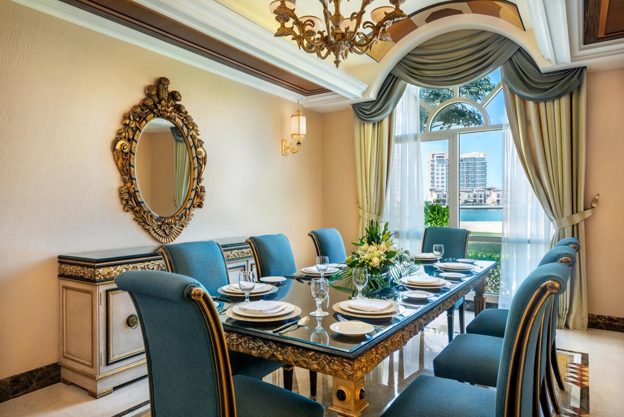 אבו דאבי Al Raha Beach Resort & Spa מראה חיצוני תמונה The photo features an elegantly decorated dining room. It includes a long, polished table set for a meal with plates, glasses, and decorative items, surrounded by plush blue chairs. The room is adorned with sophisticated details, such as an ornate mi