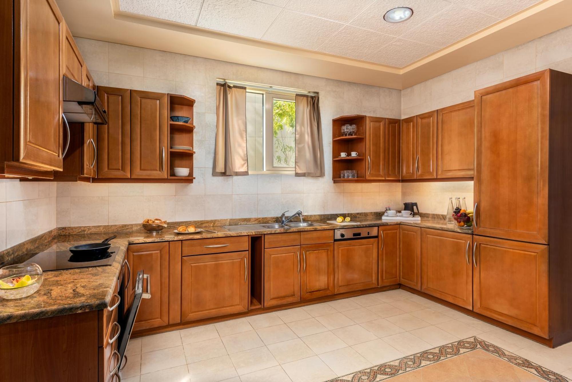 אבו דאבי Al Raha Beach Resort & Spa מראה חיצוני תמונה The photo shows a cozy kitchen featuring wooden cabinets with a rich brown finish, providing a warm and inviting atmosphere. The countertops are made of a light-colored stone, complementing the cabinetry. There is a window above the sink, allowing na