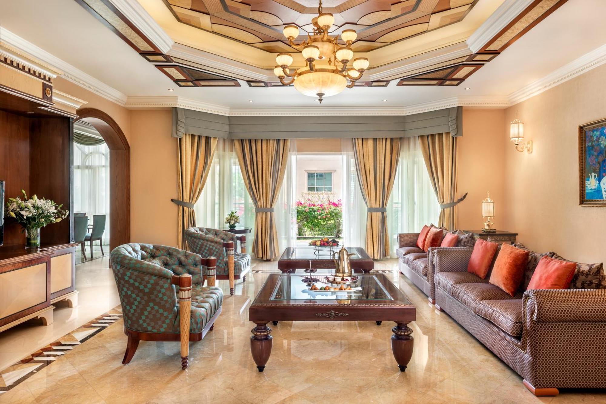 אבו דאבי Al Raha Beach Resort & Spa מראה חיצוני תמונה The photo shows an elegantly designed living room. It features a high, intricately patterned ceiling with a chandelier hanging in the center. The room is filled with natural light from large windows covered with flowing curtains. 

There are two diff