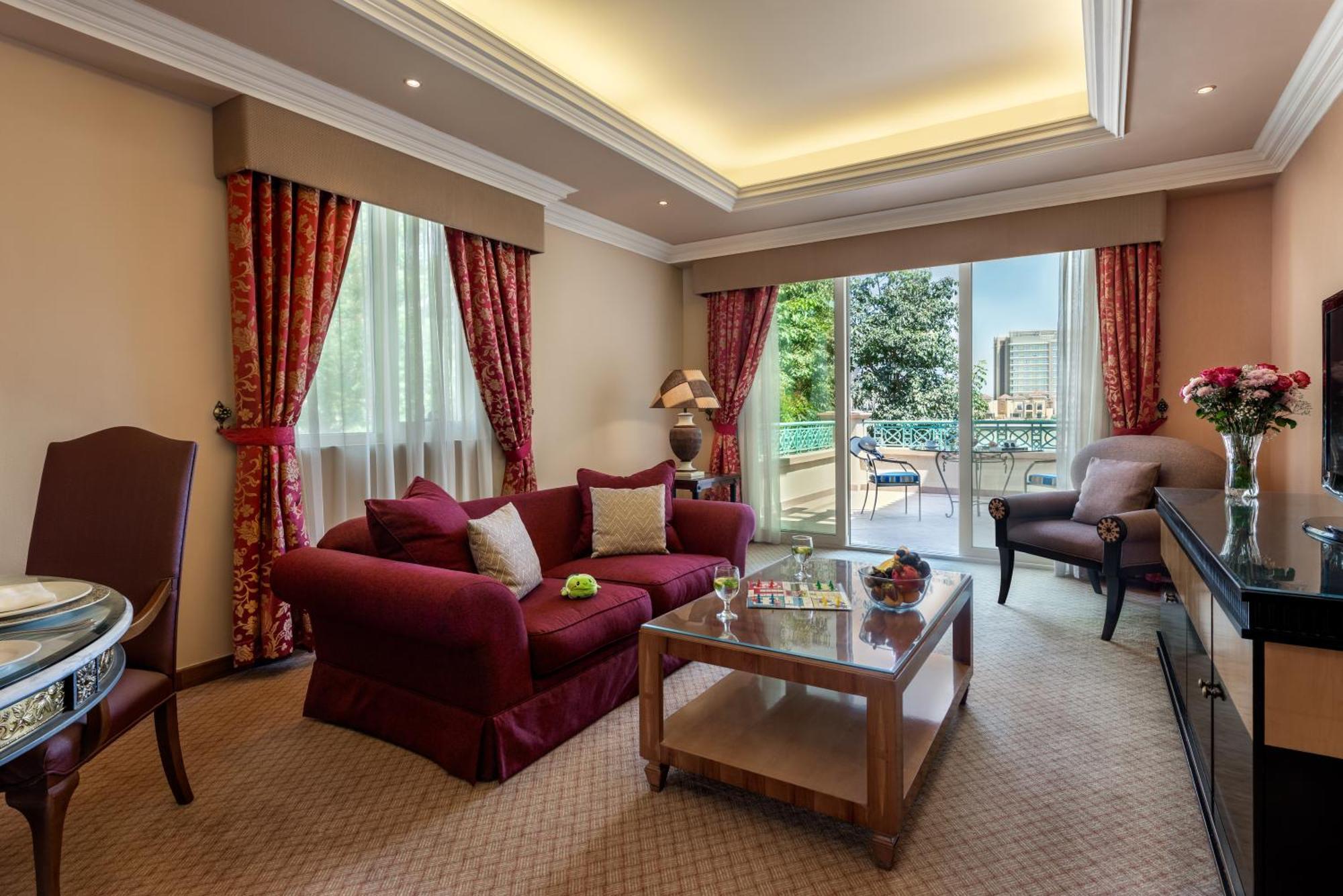 אבו דאבי Al Raha Beach Resort & Spa מראה חיצוני תמונה The photo shows a well-decorated hotel room or living area. It features a cozy seating arrangement with a deep red couch adorned with cushions, paired with a single chair. There is a glass coffee table in front of the couch, which is set on a plush c
