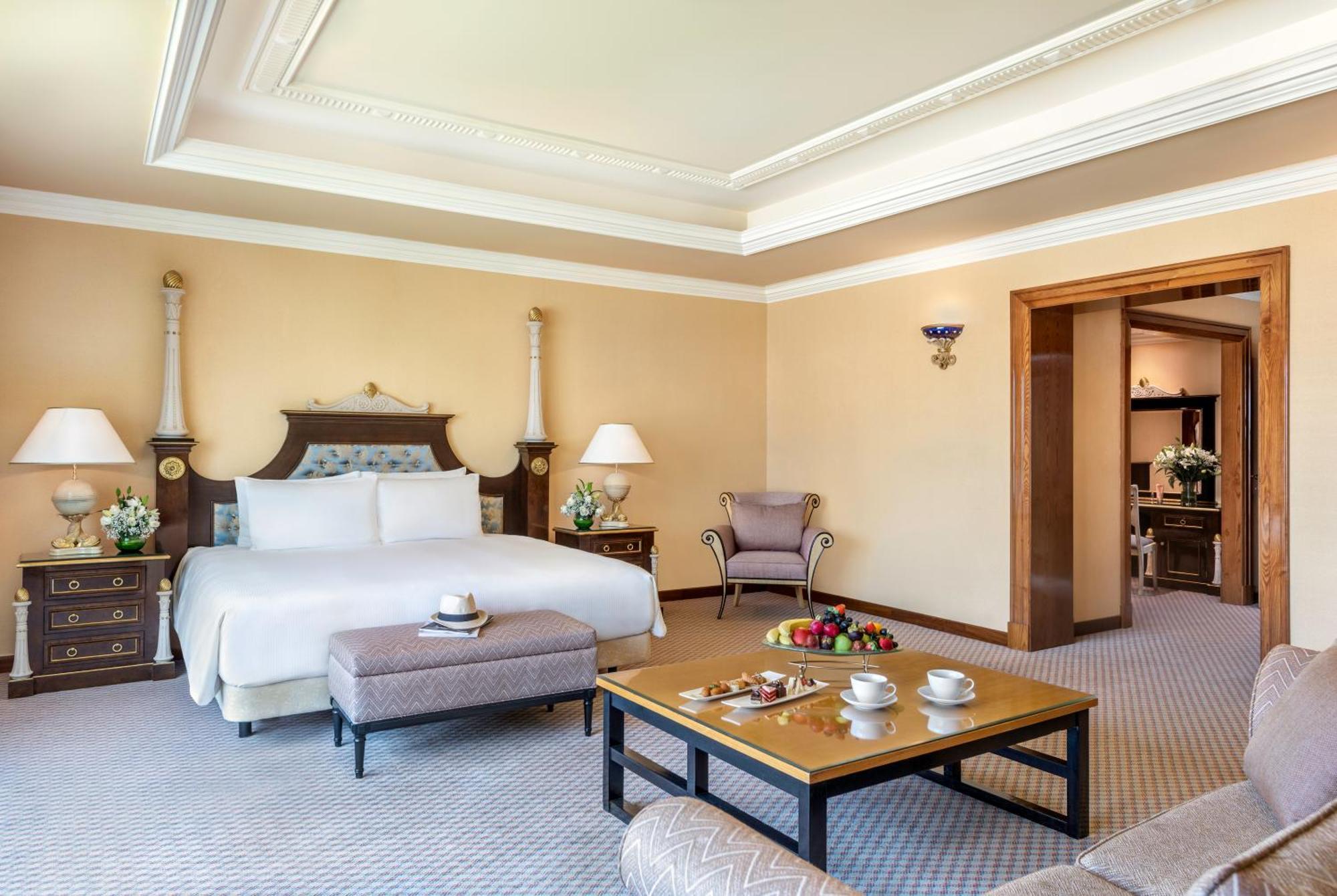אבו דאבי Al Raha Beach Resort & Spa מראה חיצוני תמונה The photo shows an elegant hotel room, featuring a large bed with white linens, flanked by stylish bedside tables and lamps. The room has a warm color palette, with light brown walls and a plush carpet. A comfortable armchair is positioned nearby, an