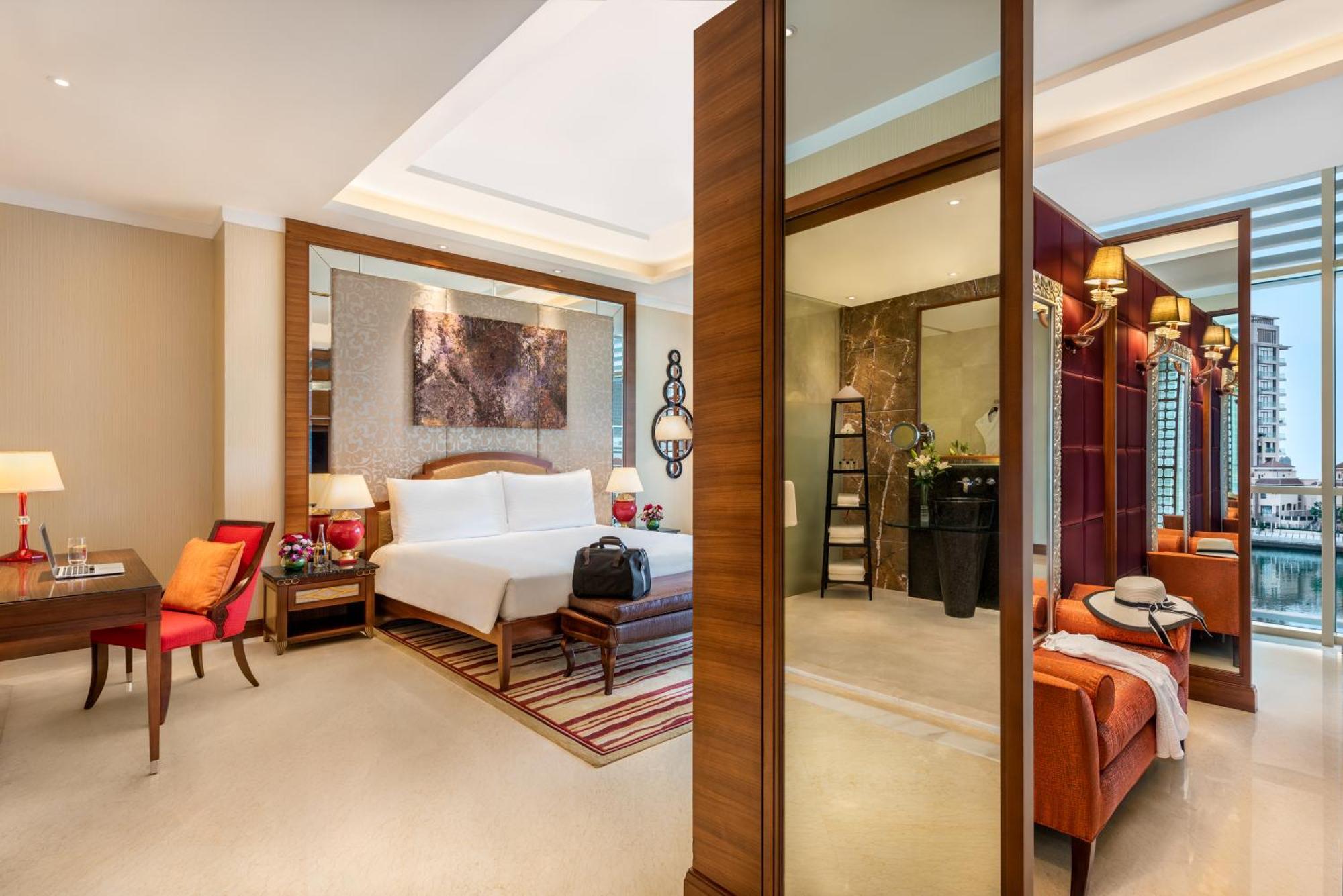 אבו דאבי Al Raha Beach Resort & Spa מראה חיצוני תמונה The photo shows a luxurious hotel room with a modern design. The room features a large bed with white linens, flanked by bedside tables with lamps. There is a area with a chair and a small table on the left side, and a vibrant artwork hanging above t