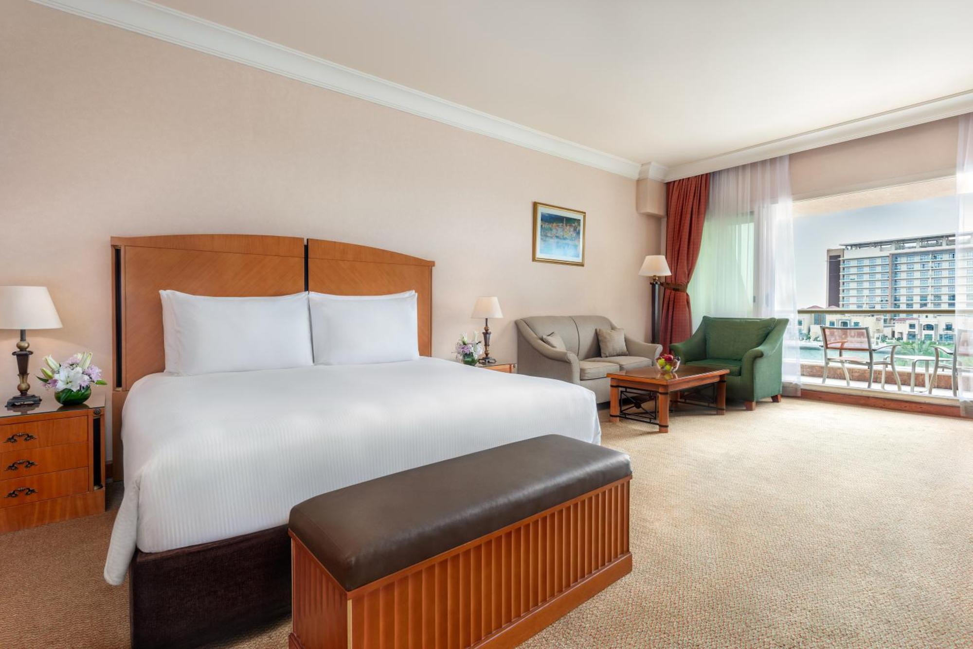 אבו דאבי Al Raha Beach Resort & Spa מראה חיצוני תמונה The photo shows a well-furnished hotel room featuring a large bed with white linens and a wooden headboard. There's a brown bench at the foot of the bed. To one side, a sitting area includes a sofa and a coffee table, complemented by two lamps. Large