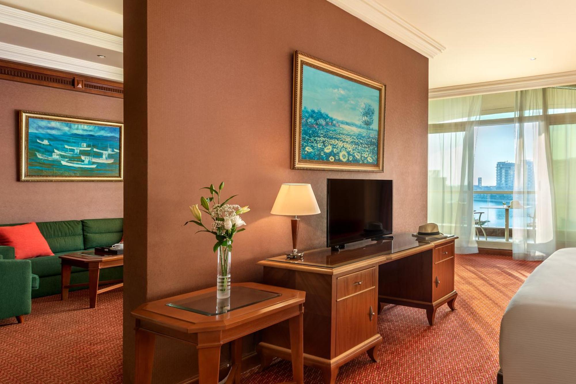 אבו דאבי Al Raha Beach Resort & Spa חדר תמונה The photo shows a hotel room with a warm, inviting atmosphere. There's a large window that provides natural light and a view, likely overlooking a cityscape or water. On one wall, there's a piece of artwork featuring a landscape, and nearby, a small 
