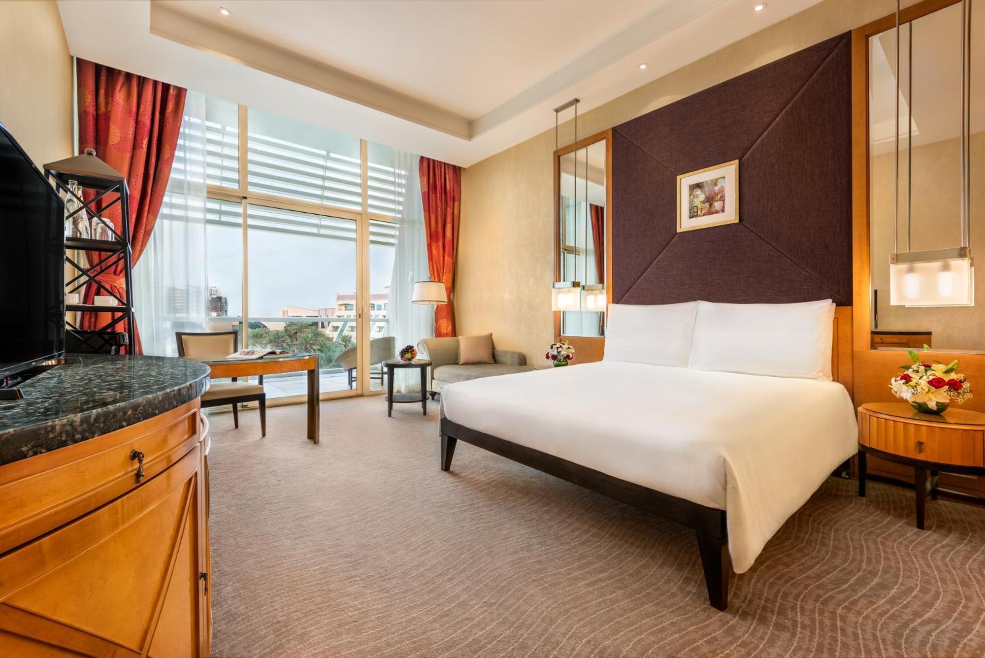 אבו דאבי Al Raha Beach Resort & Spa חדר תמונה The photo shows a modern hotel room featuring a large bed with a white duvet positioned against a purple accent wall. There are tall windows with sheer curtains allowing natural light to enter the space, along with red drapes framing the windows. A d